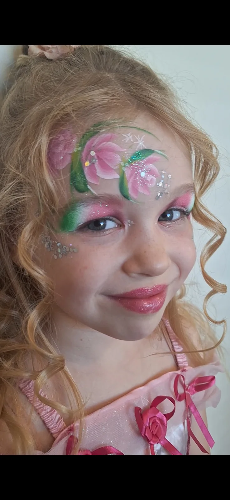 Kind met roze bloemen en glitters geschminkt rond de ogen